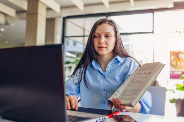 istock Young female teacher working through videoconference in office using laptop. Woman showing students book online 1974871331