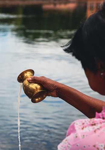 Port Louis, Mauritius - January 12, 2023: In this photo, a woman is seen pouring water from a brass faucet in a traditional Indian ritual, showcasing religious customs in Mauritius.