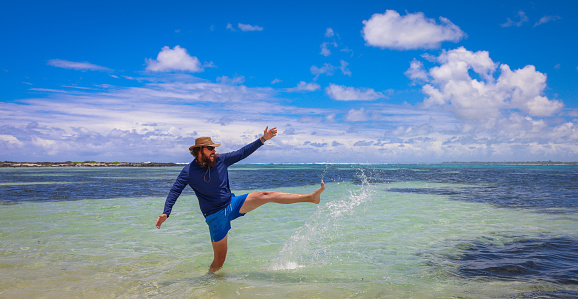 A man in Mauritius stands in the ocean, kicking up water with forceful movements.