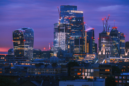 Aerial panoramic view of The City of London cityscape skyline with metropole financial district modern skyscrapers after sunset on night with illuminated buildings and cloudy sky in London, UK