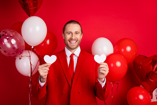 Photo portrait of elegant young male hold hearts postcards air balloons wear trendy classic garment isolated on red color background.