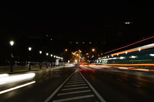 An illuminated street adorned with streetlights as hazy vehicles pass by