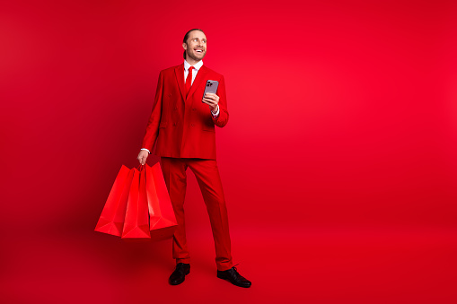 Full size photo of handsome young guy shopping device look empty space wear trendy classic outfit isolated on red color background.