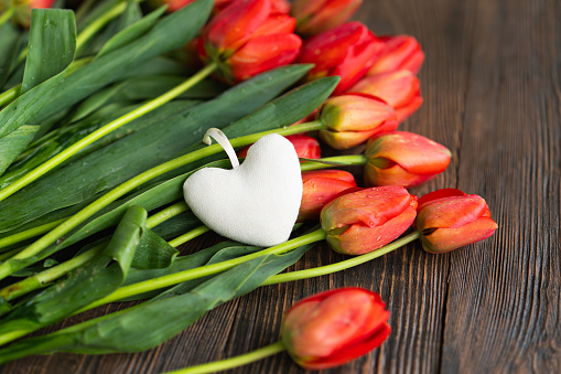 Bouquet of beautiful fresh orange tulips with gift boxe and red paper hearts on wood background. Greeting card with copy space for Valentine's Day, Woman's Day and Mother's Day.