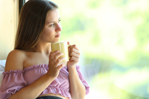 istock Teen looking through a window drinking tea 1974996078