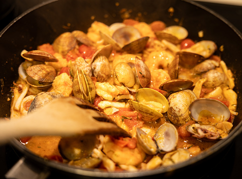 A savory seafood stew with clams, shrimp, and tomatoes simmering in a black pan.