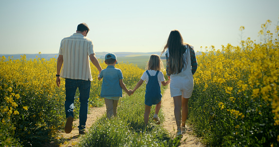 Nature, holding hands and family in canola field walking on vacation, holiday or weekend trip. Adventure, travel and back of children with parents in outdoor park with yellow flowers in countryside.