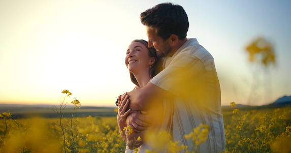 Field, sunshine and couple with love, hug and happiness with marriage and honeymoon. Countryside, man and woman with embrace and relationship with romance and vacation for anniversary and dating