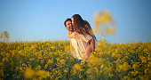 Laugh, nature field and couple piggyback ride, hug and having fun together in outdoor countryside. Blue sky, love and playful people walking, connect and bonding over funny comedy joke on honeymoon