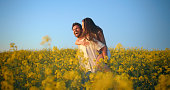 Laugh, flowers field and couple piggyback ride, hug and having fun together in outdoor countryside, nature or floral garden. Blue sky, marriage and people bonding over funny joke, humour or comedy