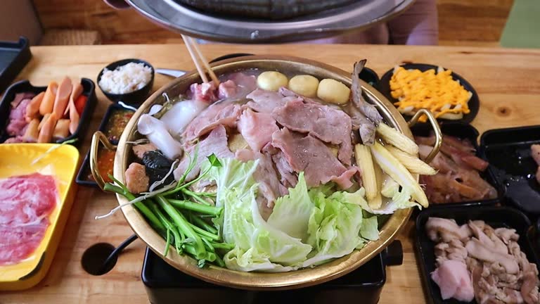 Women's hands grilling Thai BBQ (Mookata) or Korean style with many different kinds of food. with fresh food ingredients on the table