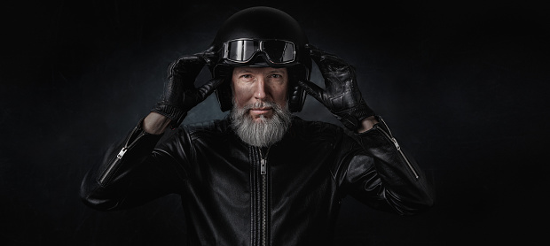 Portrait of a fifty year old biker with black helmet, protective glasses and black leather jacket on a black background