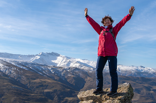 Energetic woman raises her arms in victory on a mountain summit with the Sierra Nevada in the background.