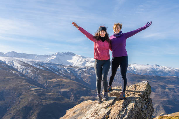 Two women friends with their arms raised in celebration on a summit in the Sierra Nevada.