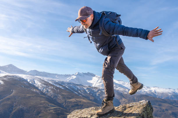 Man playfully balances on a rocky ledge with the snowy Sierra Nevada mountains stretching in the background.