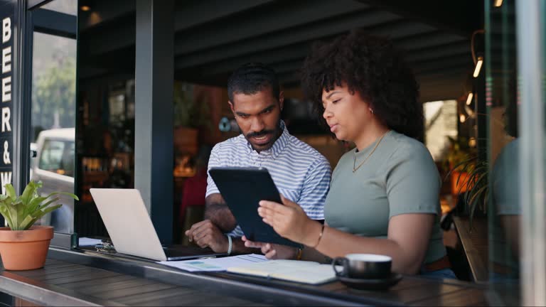 Coffee shop, workers and tablet with laptop, remote work and planning strategy for project, online or internet. People, tech and explain for freelance career, copywriters or working on social media