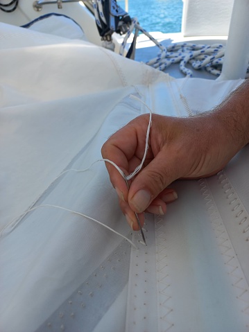 Hand stitching a sail to repair a sail onboard a sailboat with a sailing rope in the background