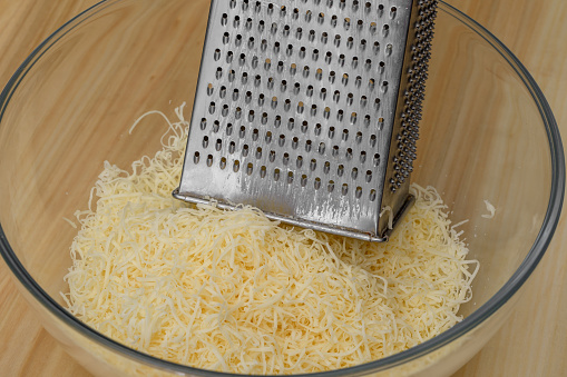 Ripening cheese grated on a kitchen steel grater into a bowl