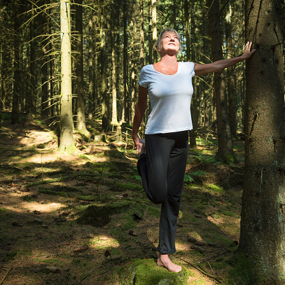 Experience the forest while bathing in the forest Shinrin Yoku with all her senses. A 50 year old woman stretches her muscles. She takes a deep breath