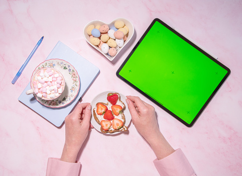 woman holding soft cheese and strawberry sandwich near green screen tablet, concept of healthy food and diet, using calorie counting app, top view, High quality photo