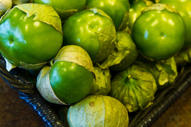 Fresh tomatillos, a staple of Mexican cuisine, sit in a woven basket, their vibrant green skins peeking out from partially peeled husks. Capturing the essence of freshness and organic growth.