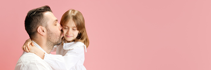 Banner. Father kissing his lovely little daughter against pink pastel background with negative space to insert text. Concept of International Day of Happiness, childhood and parenthood, positive. Ad