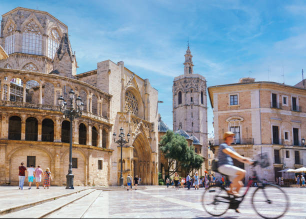 Tourist ridding bicycle through Plaza Mare de Deu with Valencia Cathedral in background Spain