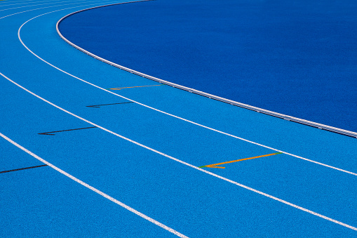 Blue Olympic track lanes with white stripes, an empty background suitable for copy space, represent the concept of physical sports and running, symbolizing commitment and pathways towards goals