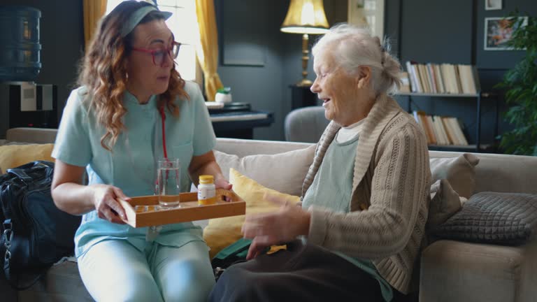 Female caregiver brings a daily dose of pills to an old woman, providing care to the elderly at home