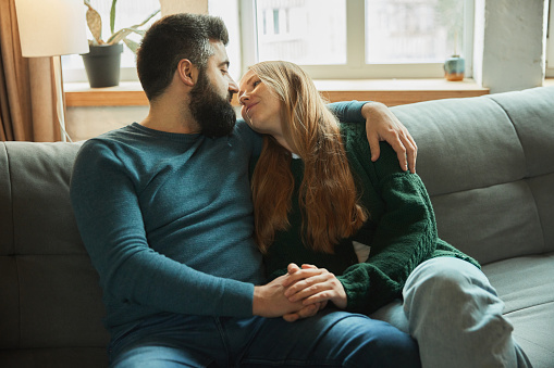 Portrait of lovely couple sitting together at home and having fun, relax together at coach in weekend day at home. Concept of togetherness, love and romantic, lifestyle, rest, relax, lifestyle.