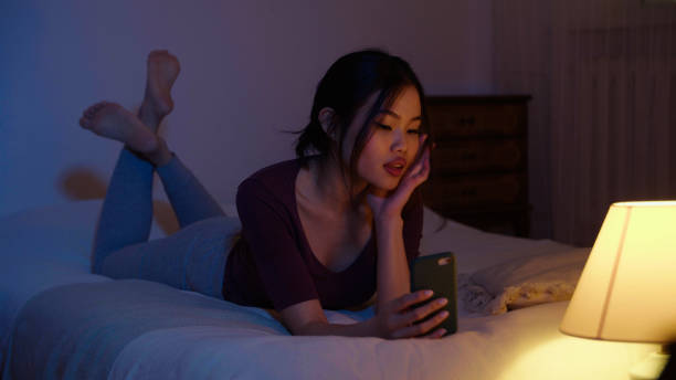 istock Happy young woman using mobile phone while lying on a bed at night. 1975221155