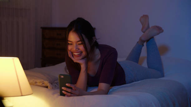 istock Happy young woman using mobile phone while lying on a bed at night. 1975221156