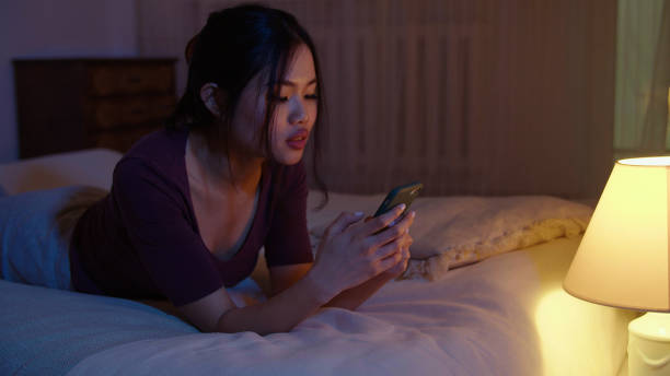 istock Happy young woman using mobile phone while lying on a bed at night. 1975221673