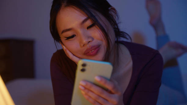 istock Happy young woman using mobile phone while lying on a bed at night. 1975221675