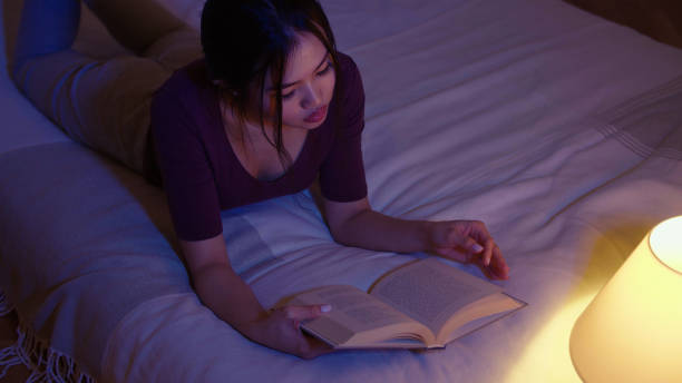 istock Young beautiful woman reading book while lying in bed at night. 1975221686