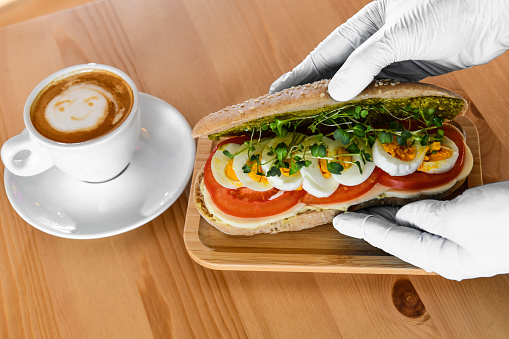 Cook Placing Egg Sandwich On Wooden Plate Right Next To Coffee With Smiley Face