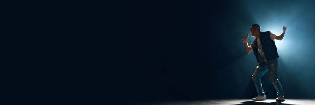 istock Banner. Man, artist singing with microphone in smoke illuminated blue stage light against dark background with negative space for text. Ad 1975242471