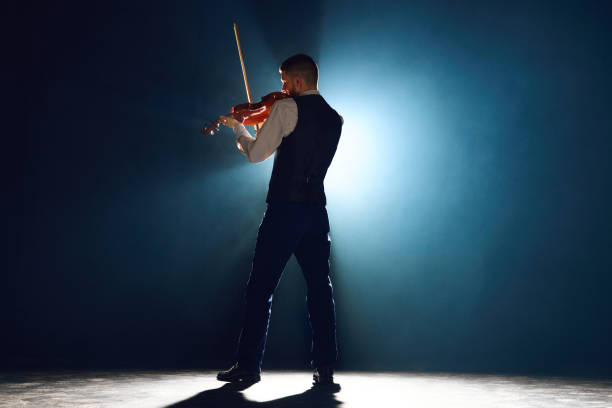 Professional musician with violin under performing his new melody on stage with spotlights showcasing classical music's allure. Concept of instrumental music festivals and concerts, art, culture. Ad