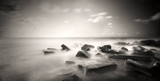 A black and white photograph, taken using long exposure technique, depicting the square-shaped rocks submerged in the sea. stock photo