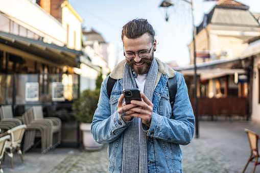 Cheerful modern young man using smart phone outdoors