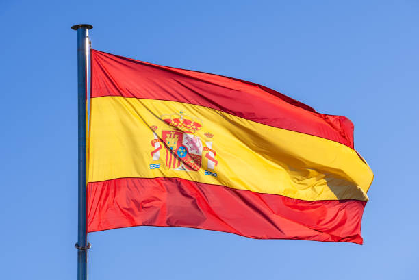 istock Spanish flag waves in the wind against a blue sky, banner blowing like soft silk 1975258454