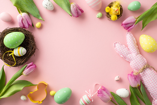 Easter magic unfolding. Overhead shot featuring bright eggs, playful cookie cutter, charming bunny, nest, chicken, tulips on a soft pink background. Excellent for text or advertising