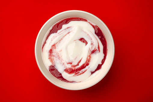 Bowl of yogurt with berry jam swirl on red background with copy space, top view