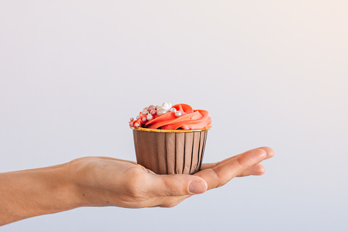 Hand with cupcake on top decorated with buttercream and sprinkles on a white background