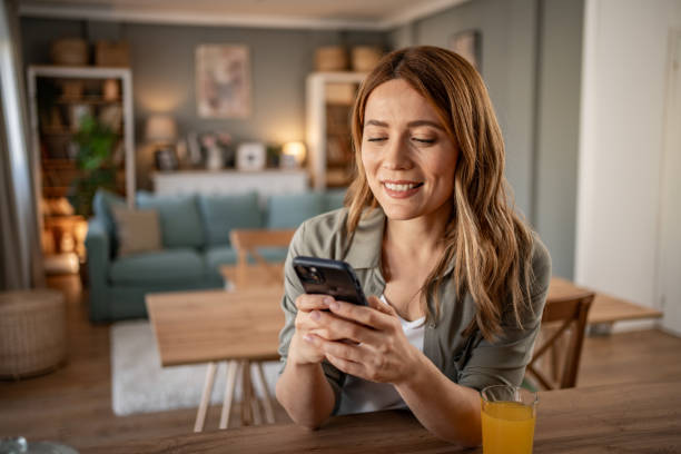 A young woman uses a mobile phone reading the latest news while preparing for breakfast This photo suggests a peaceful start to the day, devoid of everyday stress, where a woman enjoys the moment and a free weekend in her home. people using mobile phone stock pictures, royalty-free photos & images