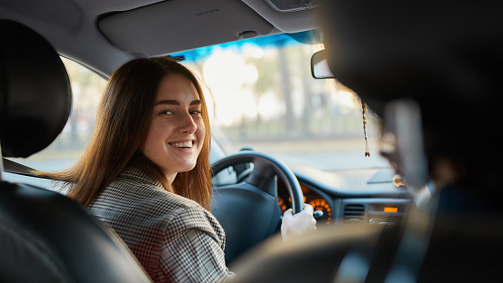 Joyful young woman sitting in a car, looking at the camera, expressing joy and excitement for obtaining her drivers license. Lifestyle and success concept