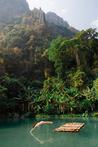Woman diving into the water from the raft on the lake surrounded by tropical mountains