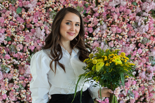 Smiling lady with yellow flower bouquet against blooming background. Beautiful woman portrait