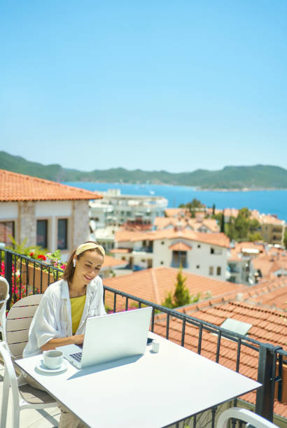 istock Pretty girl sitting on terrace during vacation on Turkish resort, using laptop computer 1975369454