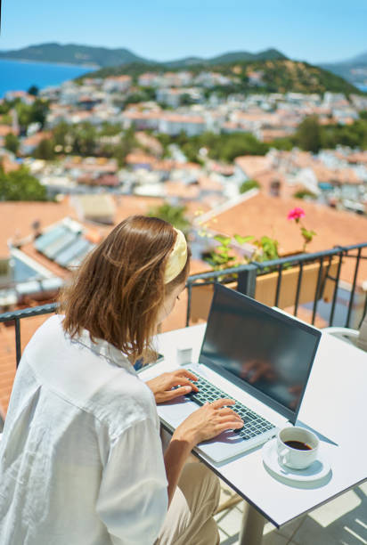 istock Rear view woman using laptop computer working typing online over Mediterranean view from outside balcony 1975371024